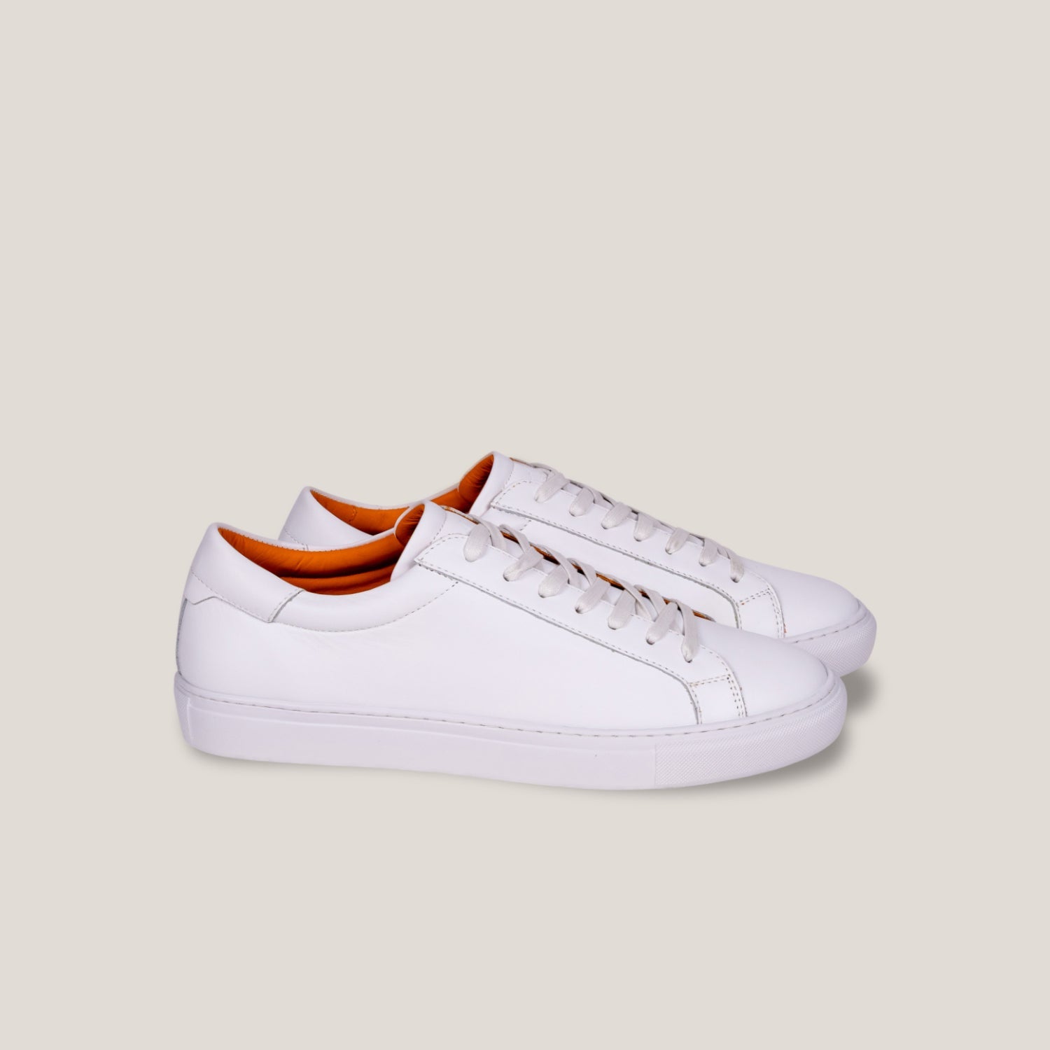 White leather sneakers with orange lining on a light gray background