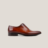 A single cognac brown patina leather Oxford shoe with a whole cut design, displayed against a plain background.